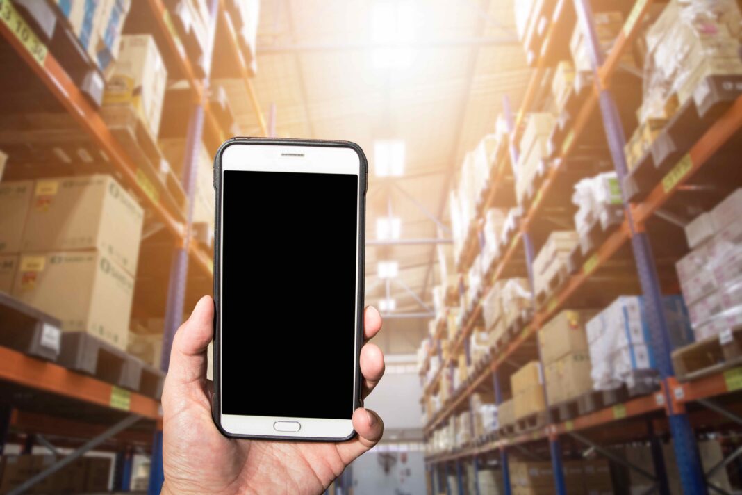 Hand holding a smartphone with black screen at warehouse, Concept for logistics management with technology
